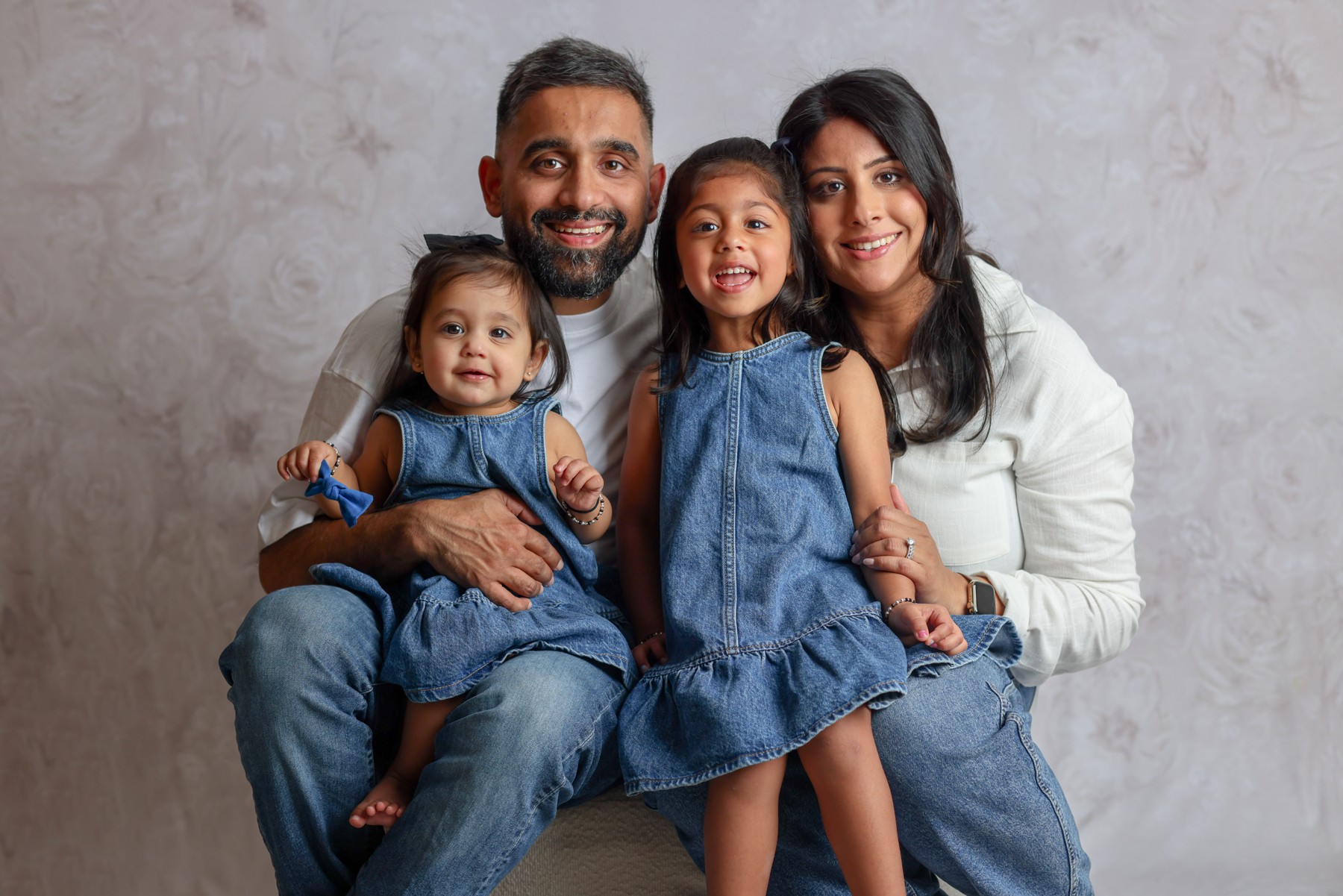 Parents embracing their two daughters in coordinated denim and ivory against a neutral studio backdrop