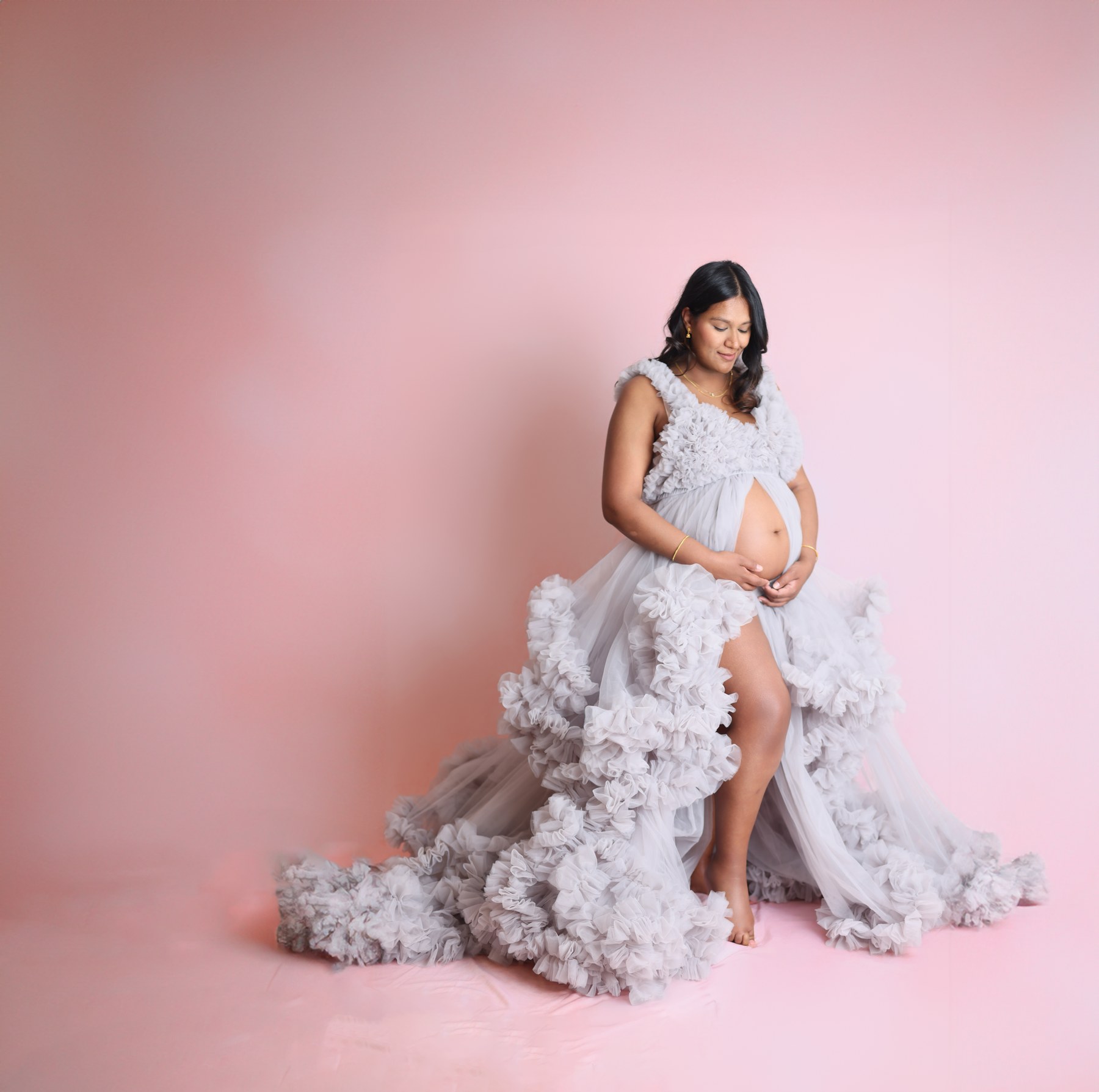 An expectant mother looking down in a lavender ruffled gown against pink