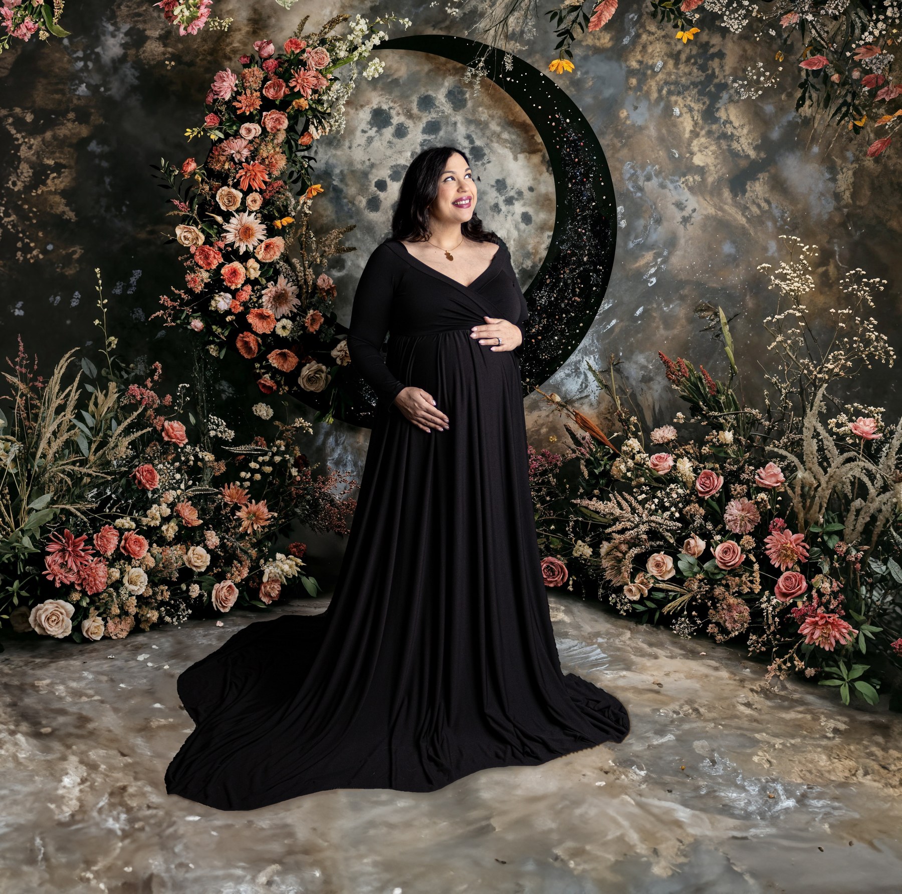 Maternity portrait in a black gown beside a floral crescent moon