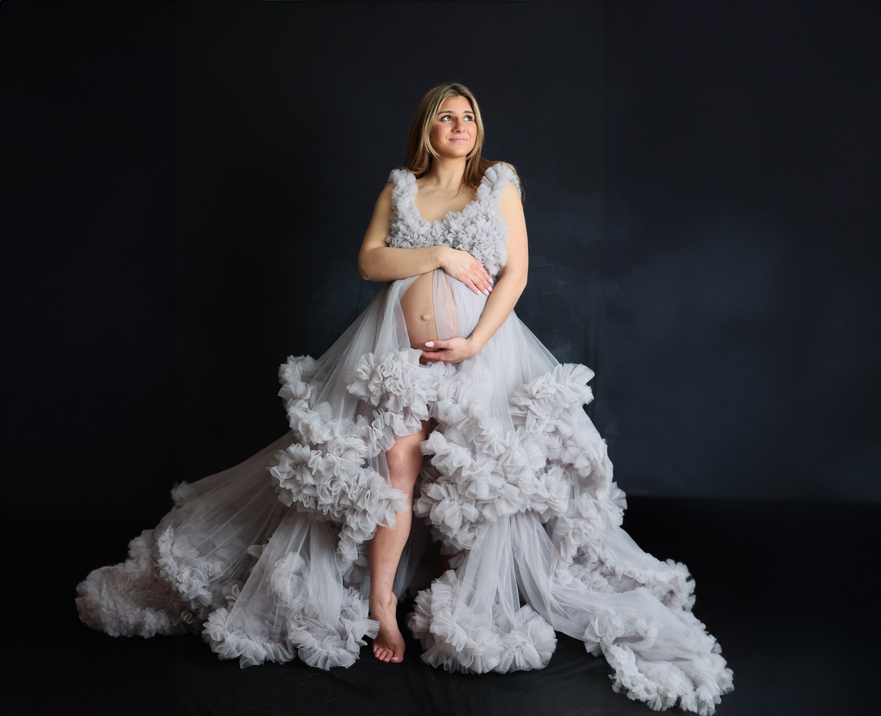 Maternity portrait in a pale ruffled gown against a black studio backdrop