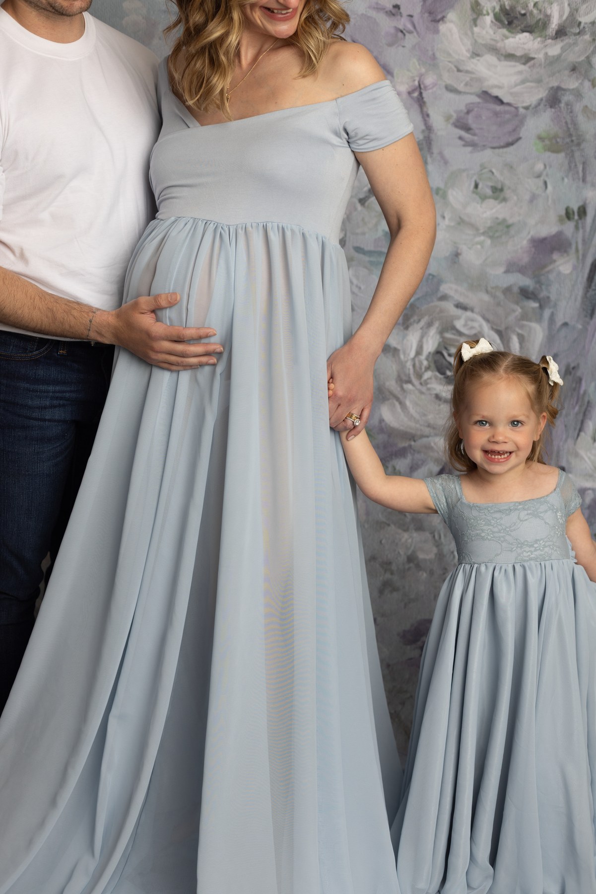 Family maternity detail with a child holding her mother’s hand in matching blue dresses