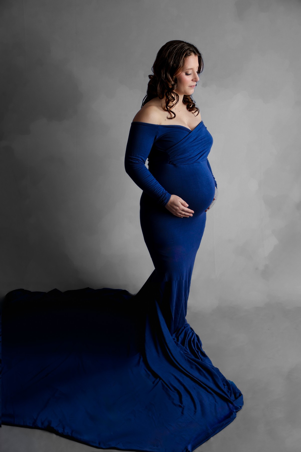 An expectant mother in a fitted navy maternity gown with a flowing train